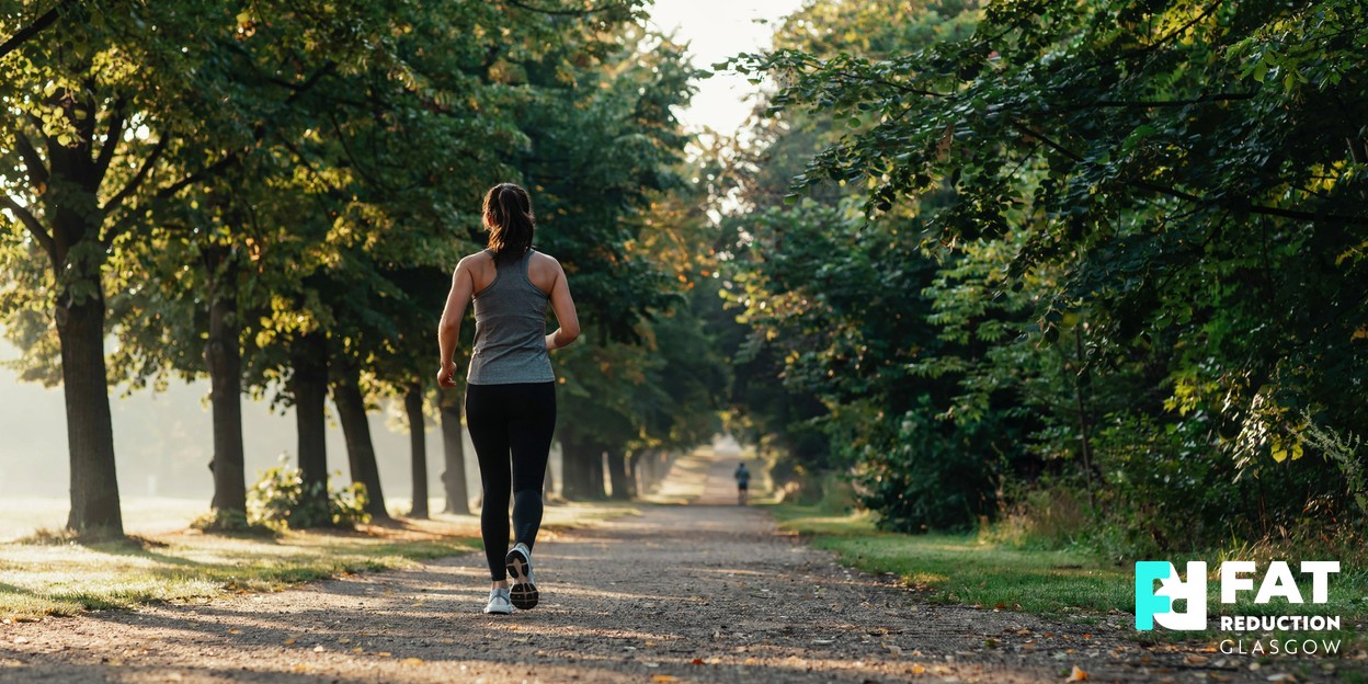 A person in athletic wear walking briskly along a tree-lined path in soft morning light, seen from behind