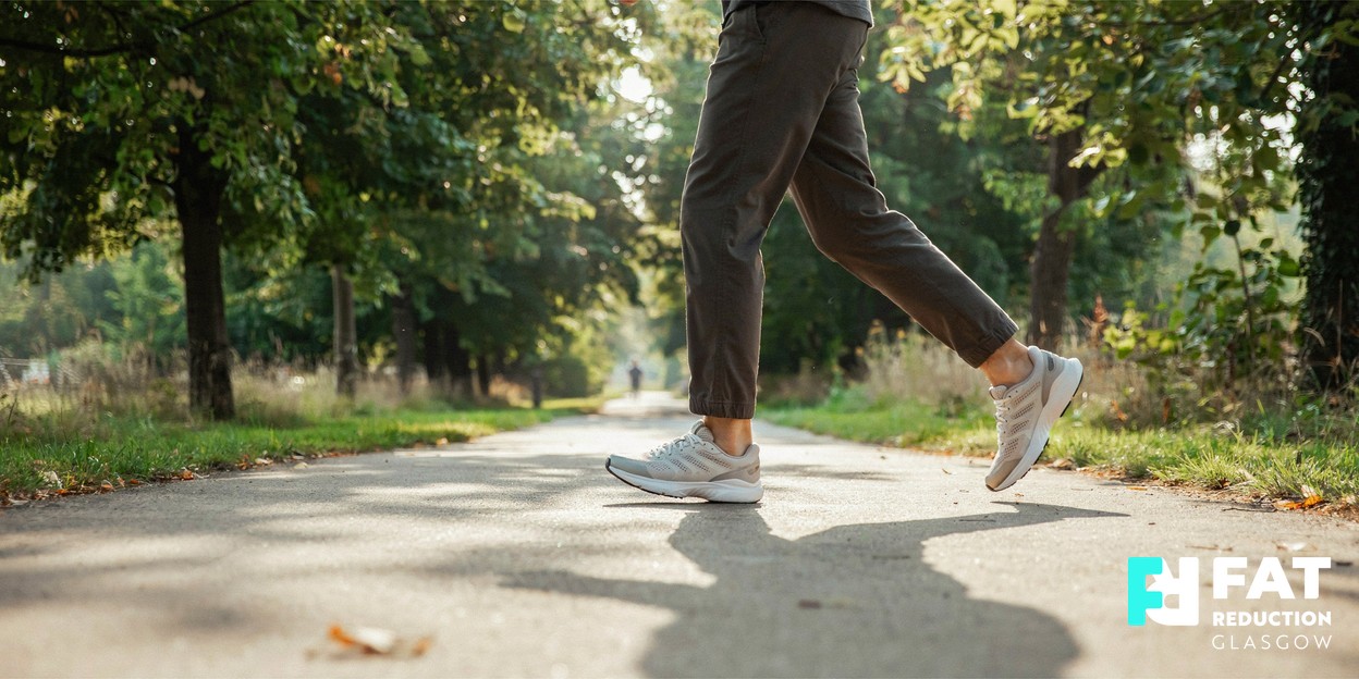 A person in trainers walking briskly along a leafy path in soft morning daylight